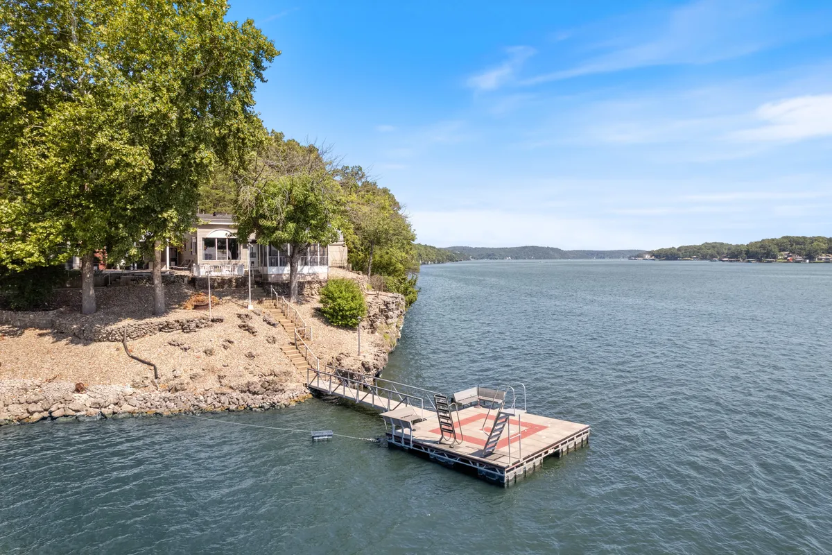 This image captures the house perched on a gentle cliff above the lake, showcasing a private dock that extends into the calm water. Surrounded by lush trees, the scene exudes peace and seclusion while highlighting direct lake access for fishing, boating, and lakeside relaxation.