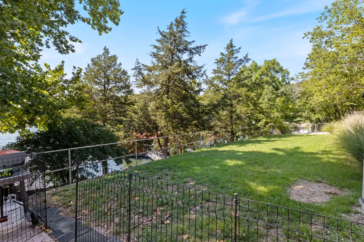 A lush, grassy yard bordered by a fence, with a distant view of the water. The open space is ideal for outdoor games, picnics, or lounging, with greenery creating a private, inviting atmosphere. The sunset glow adds warmth and charm to the setting.