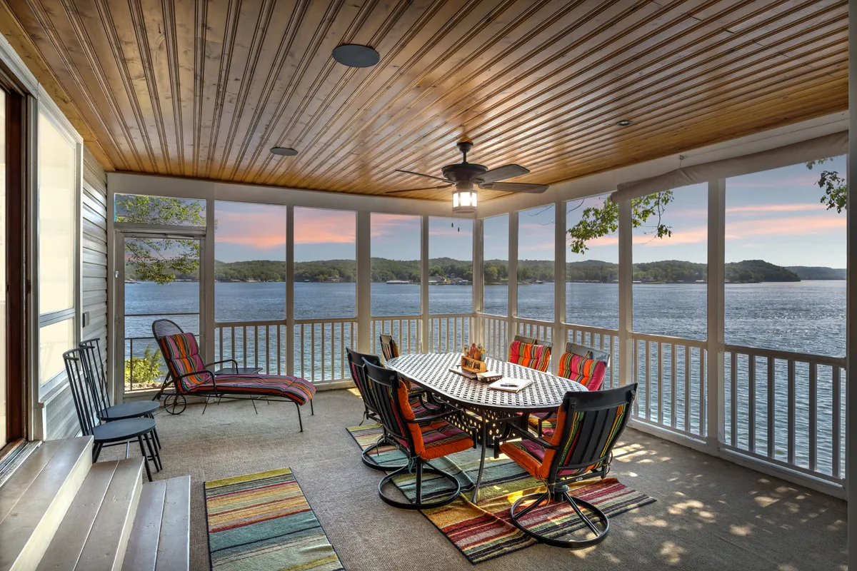 An inviting outdoor dining area with a large table and colorful chairs overlooks the lake. The covered patio provides shade while offering stunning lake views, making it a prime spot for family meals, sunset dinners, or morning coffee together.