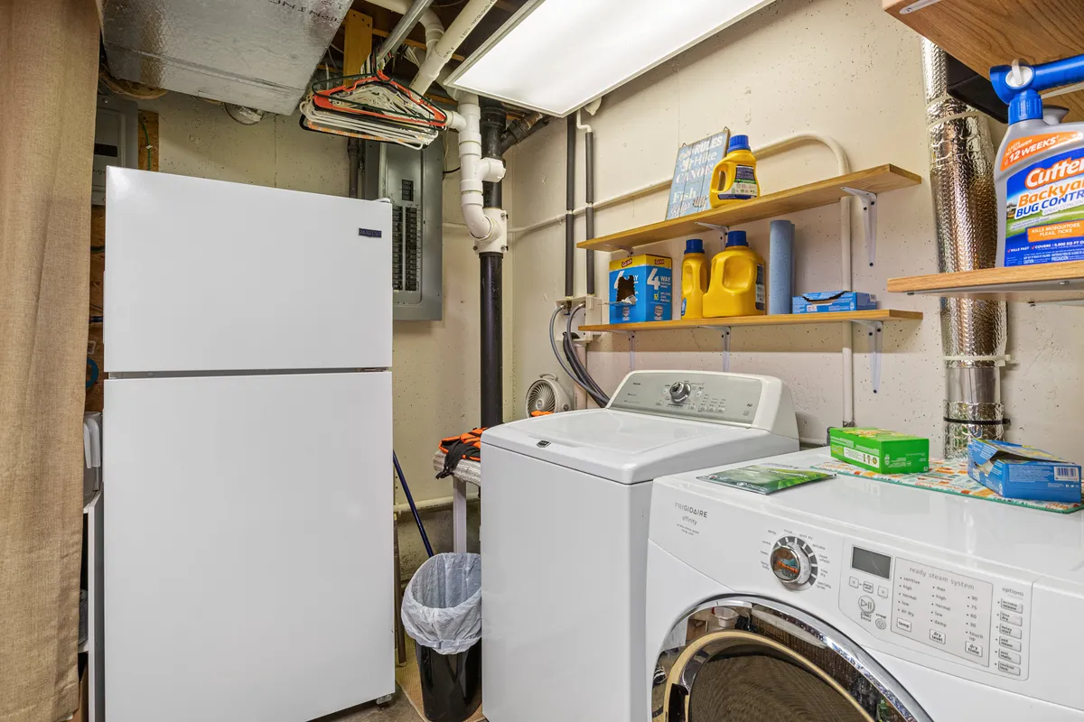 A laundry and utility area equipped with a washing machine, dryer, refrigerator, and ample shelving for supplies. The space is organized and practical, suggesting convenience for extended stays and ease in managing daily tasks.