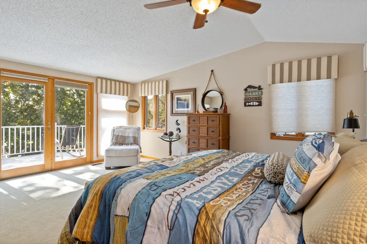 A serene bedroom with a comfortable bed adorned with colorful bedding, large windows letting in ample natural light, and a dresser with decorative items. The space exudes calm and is ideal for unwinding after a day outdoors.